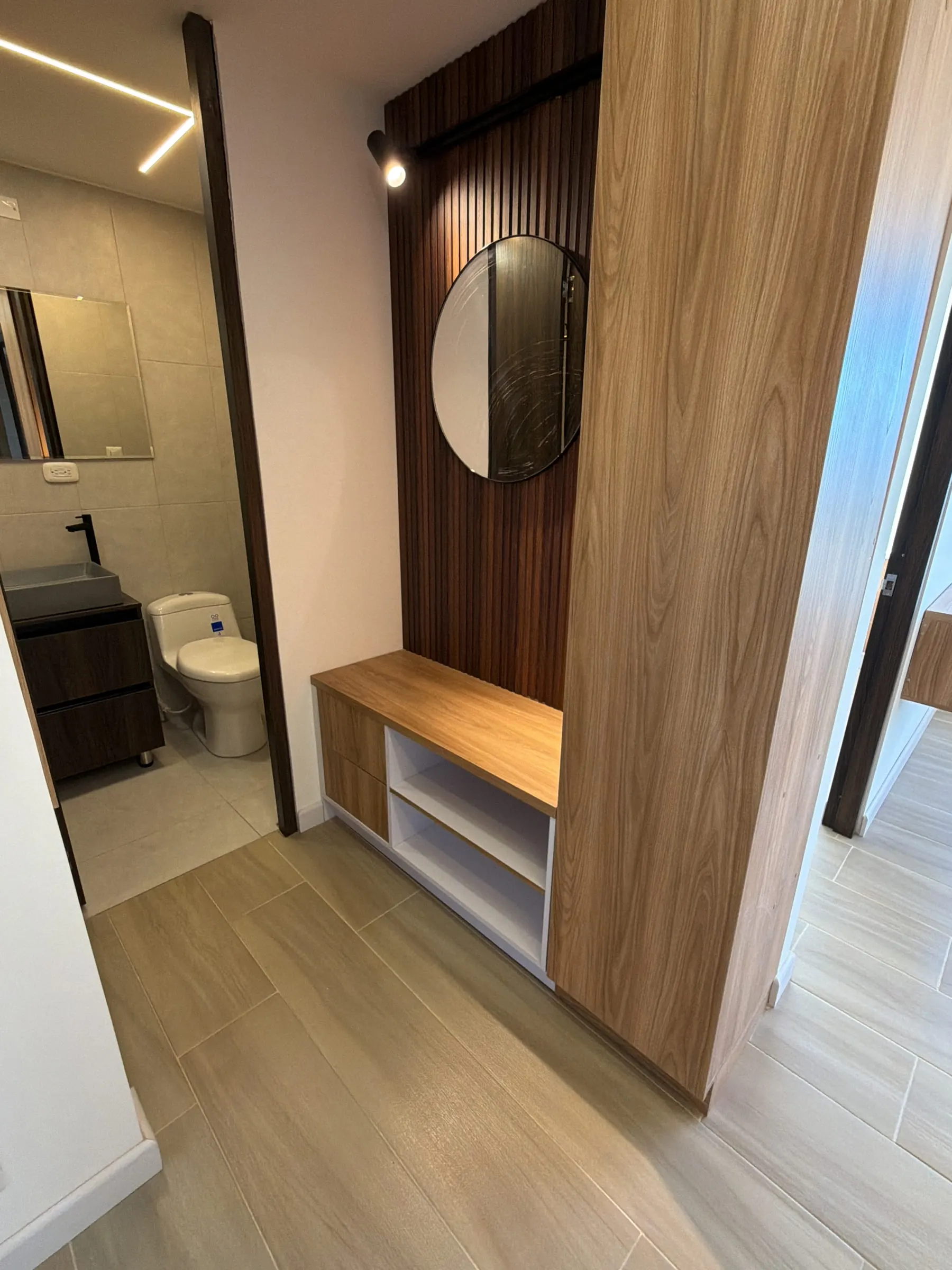 Mueble recibidor en madera con espejo redondo y banca con almacenamiento.