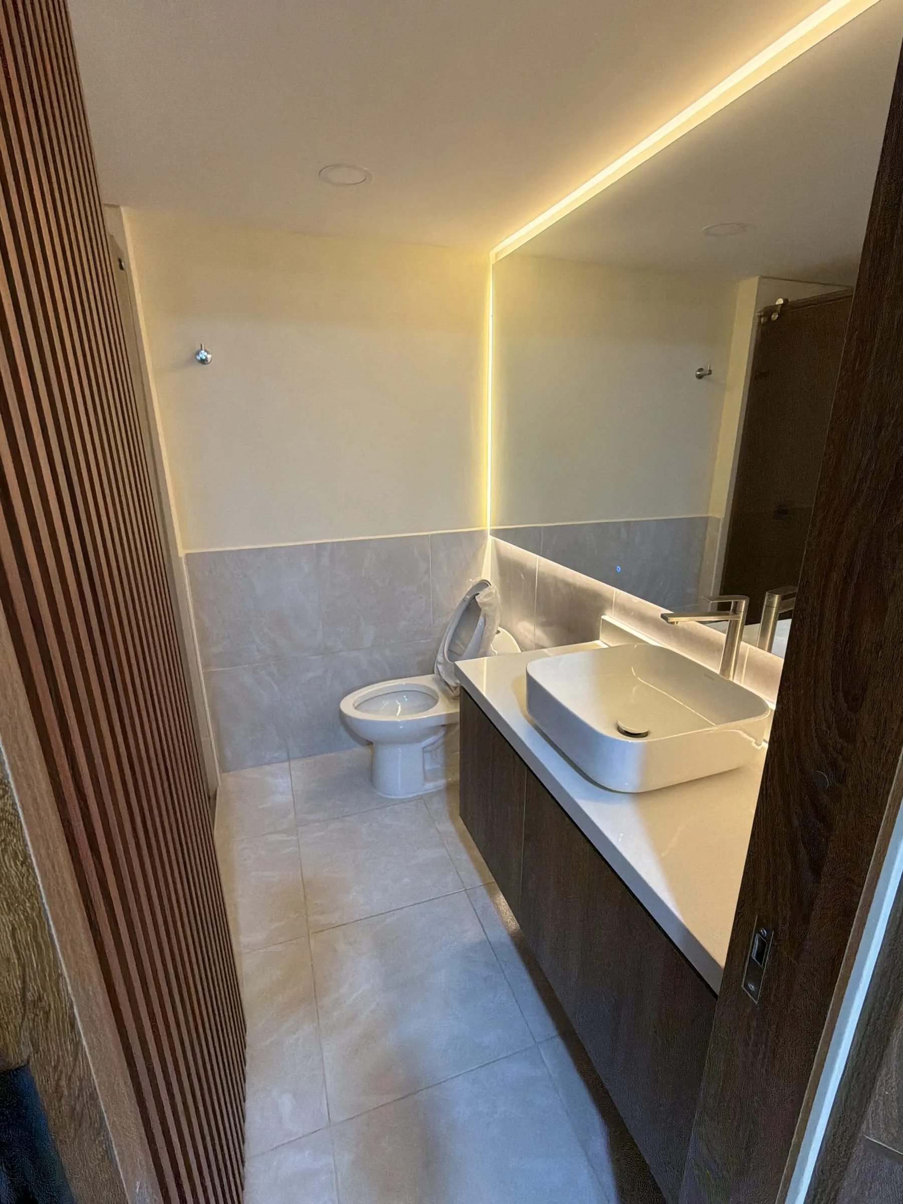 Baño con espejo iluminado y mueble en madera, acabado aprobado.